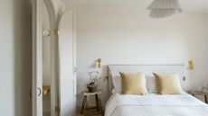 A minimalist bedroom with a low bed, a natural bedscape, a side wood stool with a vase of stems, gold wall sconces, and a pleated pendant light