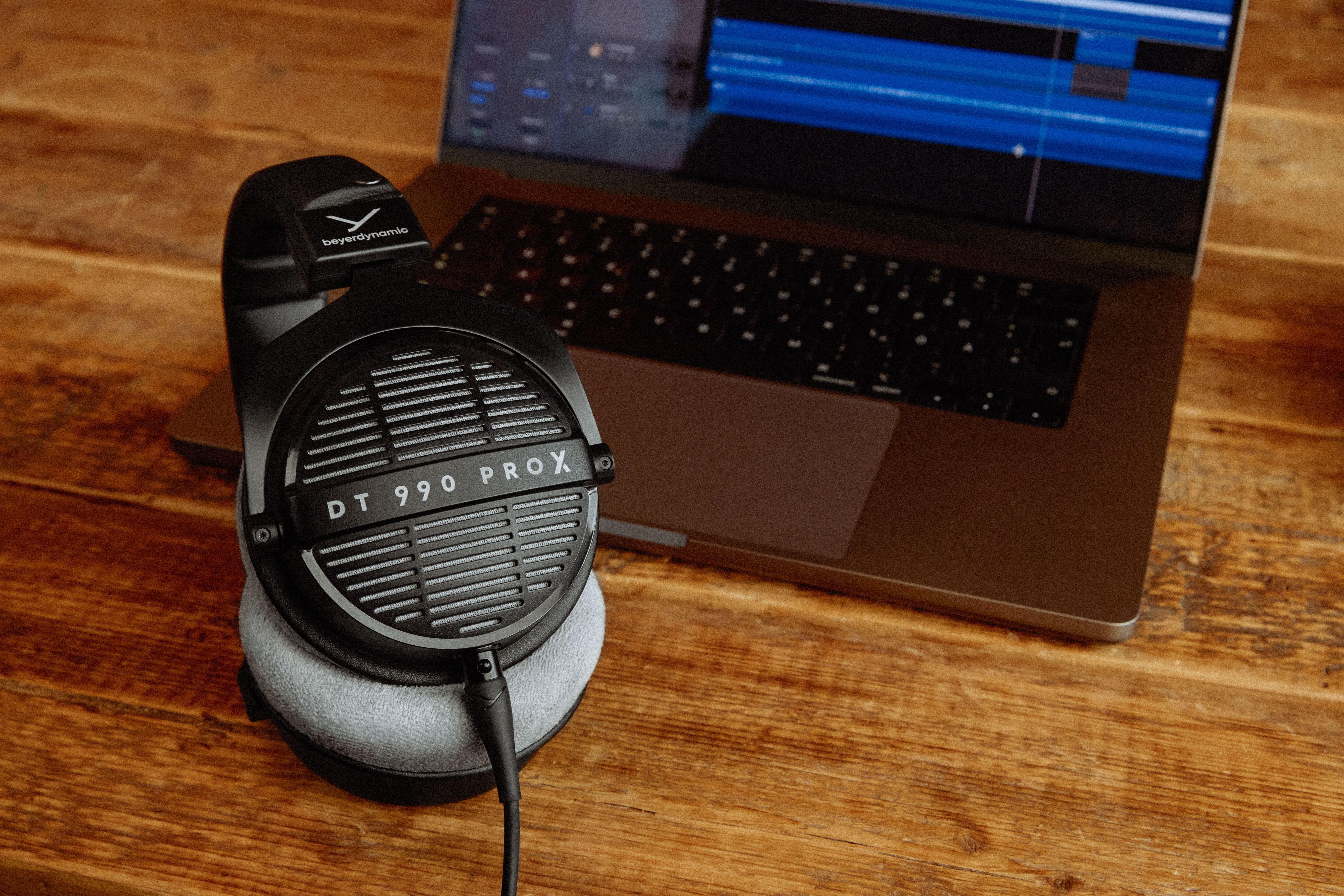 Lifestyle image for the Beyerdynamic DT-990 Pro X headphones showing the headphones in front of a laptop computer running a music app