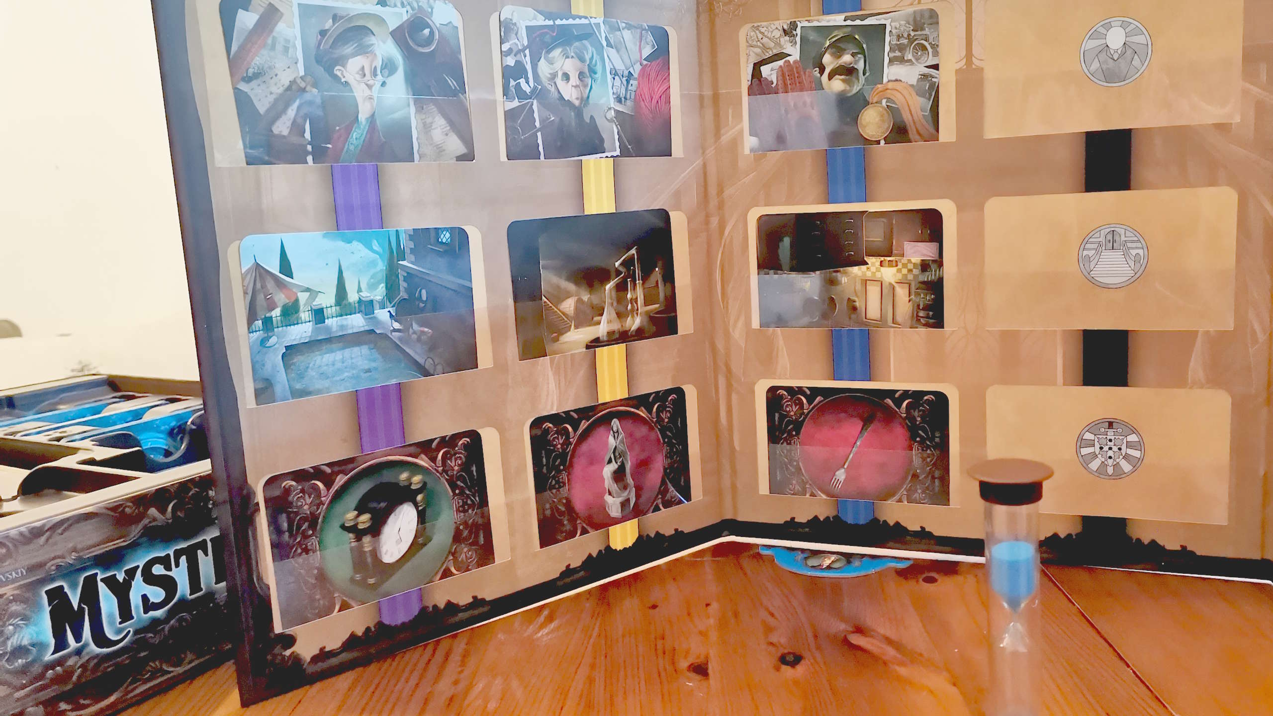 The Mysterium player clue board, with suspects, items, and locations visible behind a sand timer on a wooden surface