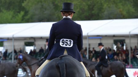 A female rider wearing a navy top hat and jacket on board a hack pictured from behind wearing number 953.