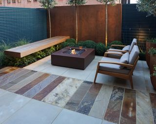 How to lay a patio shown in a sleek modern patio space with various colors of paving stone and a bronze fire pit.