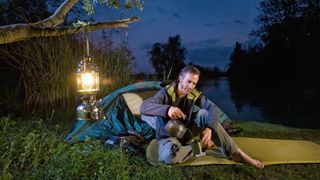 Man making coffee outside tent with camping lantern