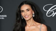 Demi Moore pictured smiling with long black curly hair over one shoulder, wearing silver circular diamond earrings