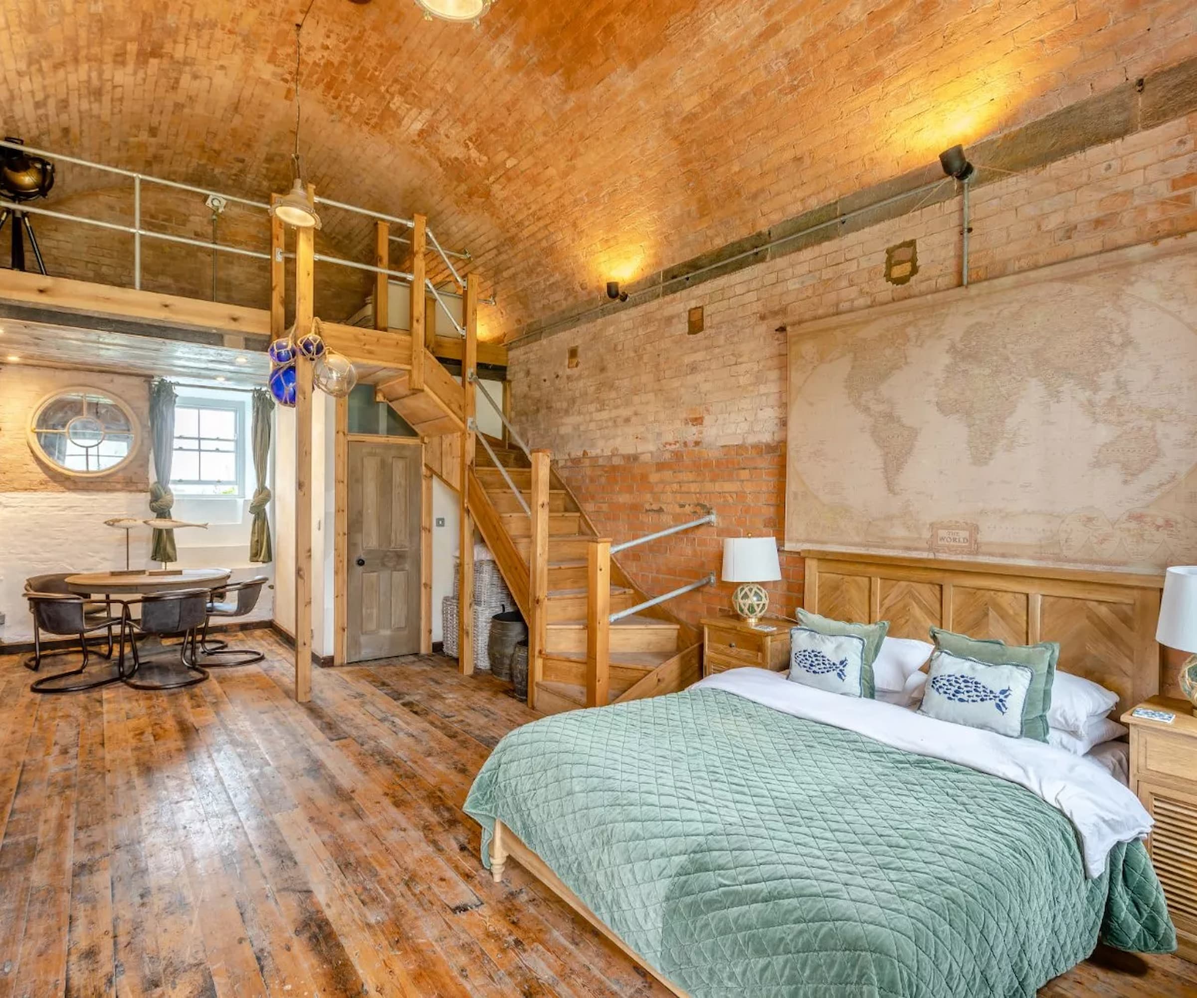 A bedroom with a mezzanine with a wooden staircase with wooden floors and a curved vaulted ceiling