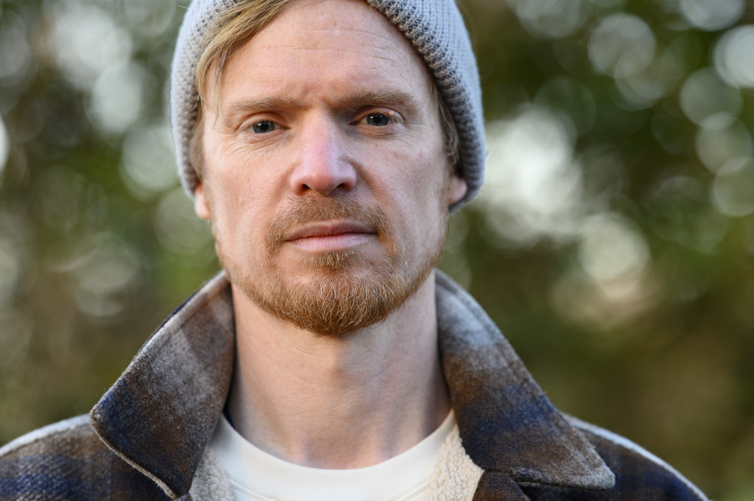 Portraits of a man in a beanie hat and shacket and golden hour with dappled light in background