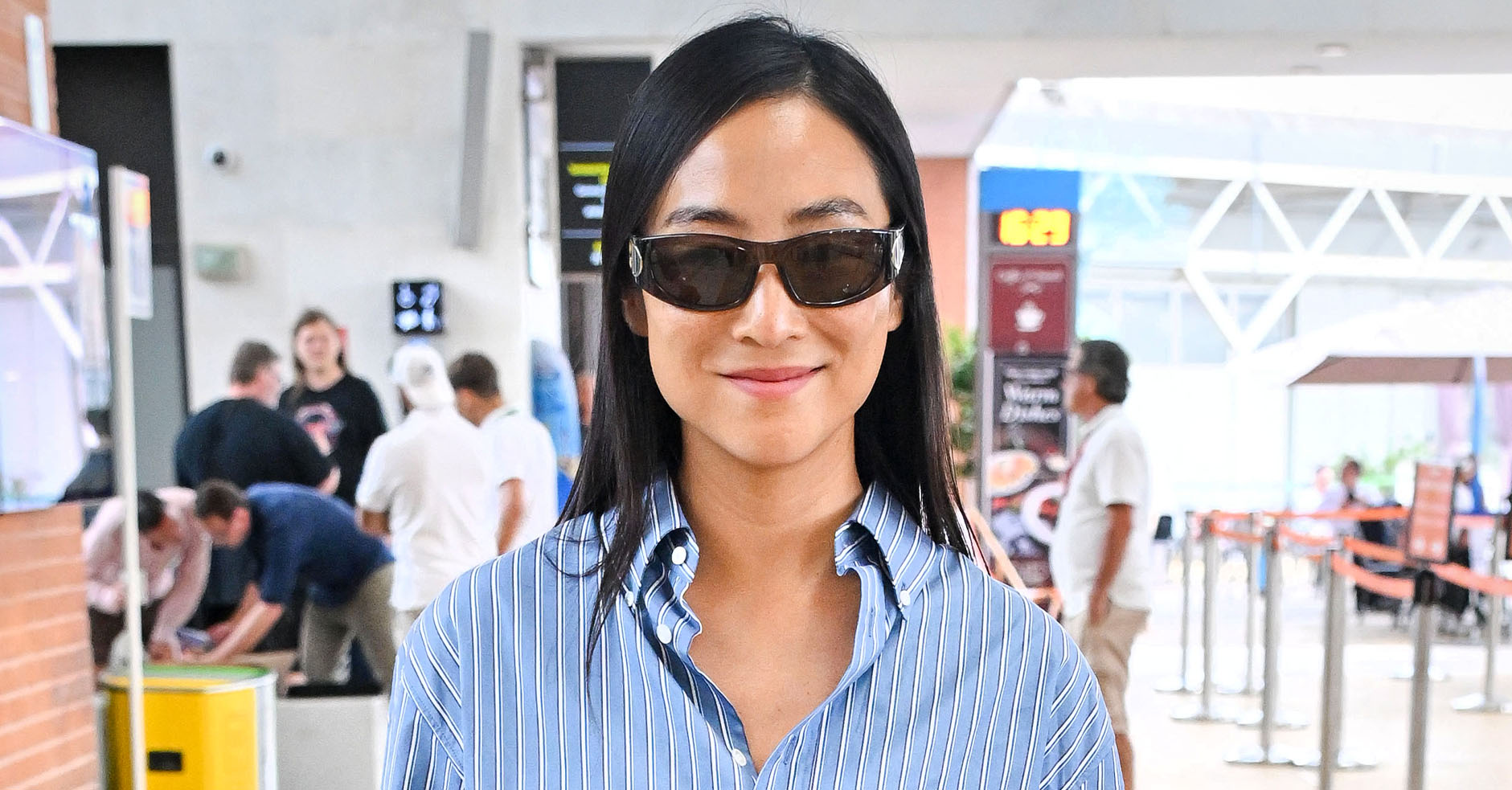 Greta Lee wearing a striped button-down shirt, blue jeans, and black boots