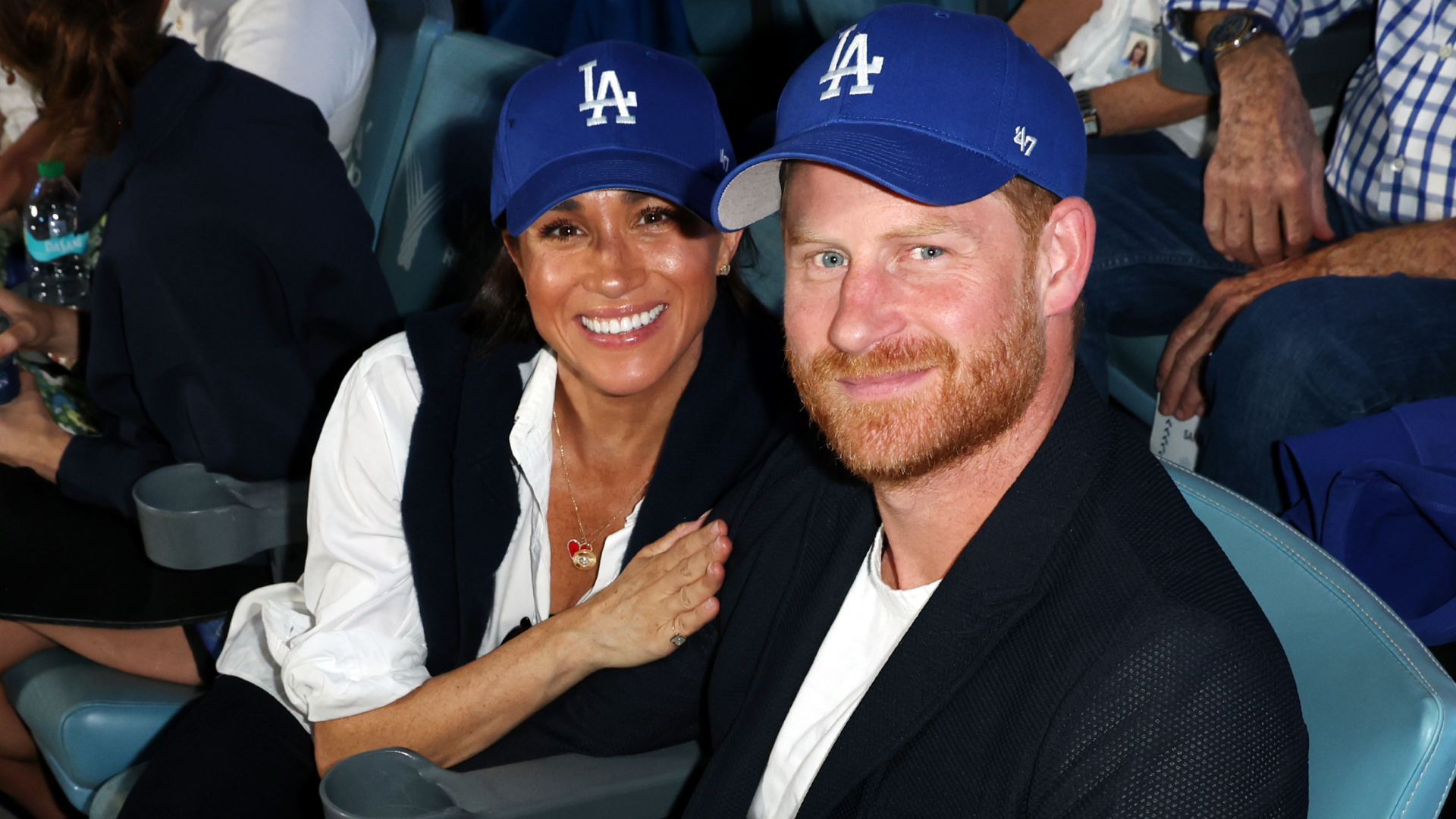 Meghan Markle and Prince Harry sitting in seats wearing Dodgers hats at the World series