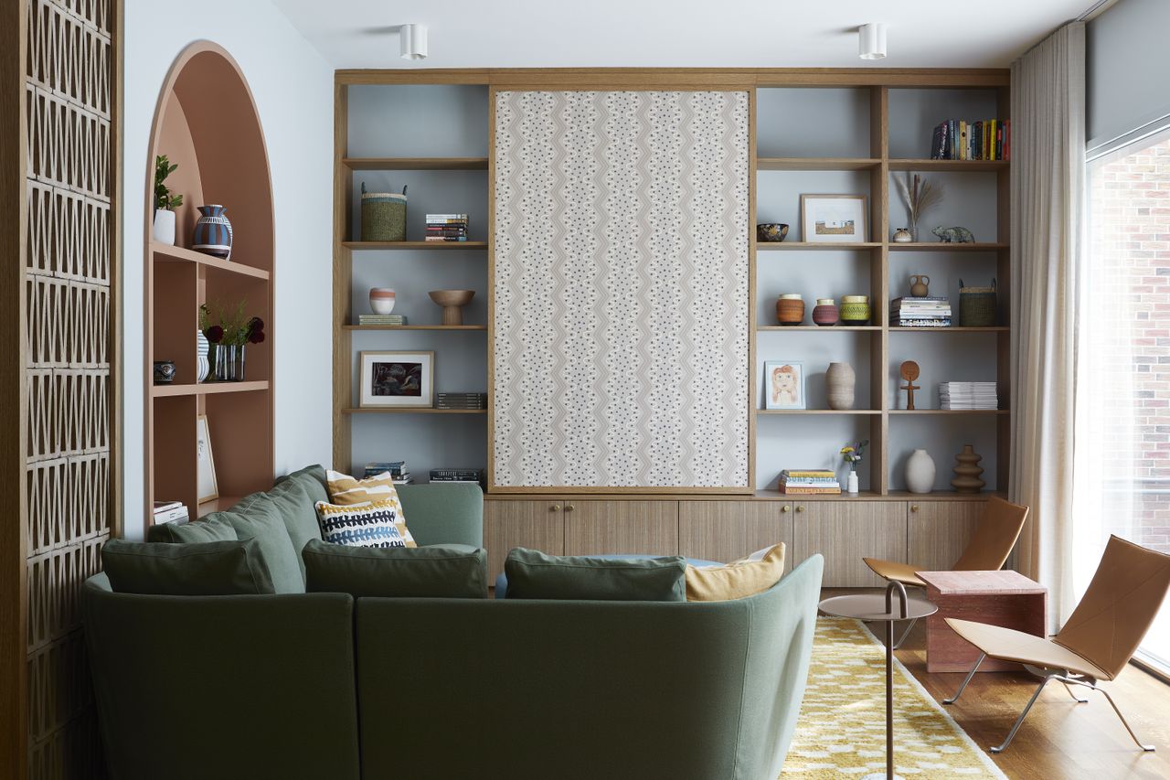 A light blue living room with green, yellow and terracotta accents a sliding panel hides the tv in built in storage