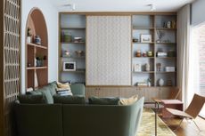 A light blue living room with green, yellow and terracotta accents a sliding panel hides the tv in built in storage