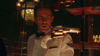 Ryan Reynolds dressed in a tuxedo gawking at a display case of guns in Red Notice.