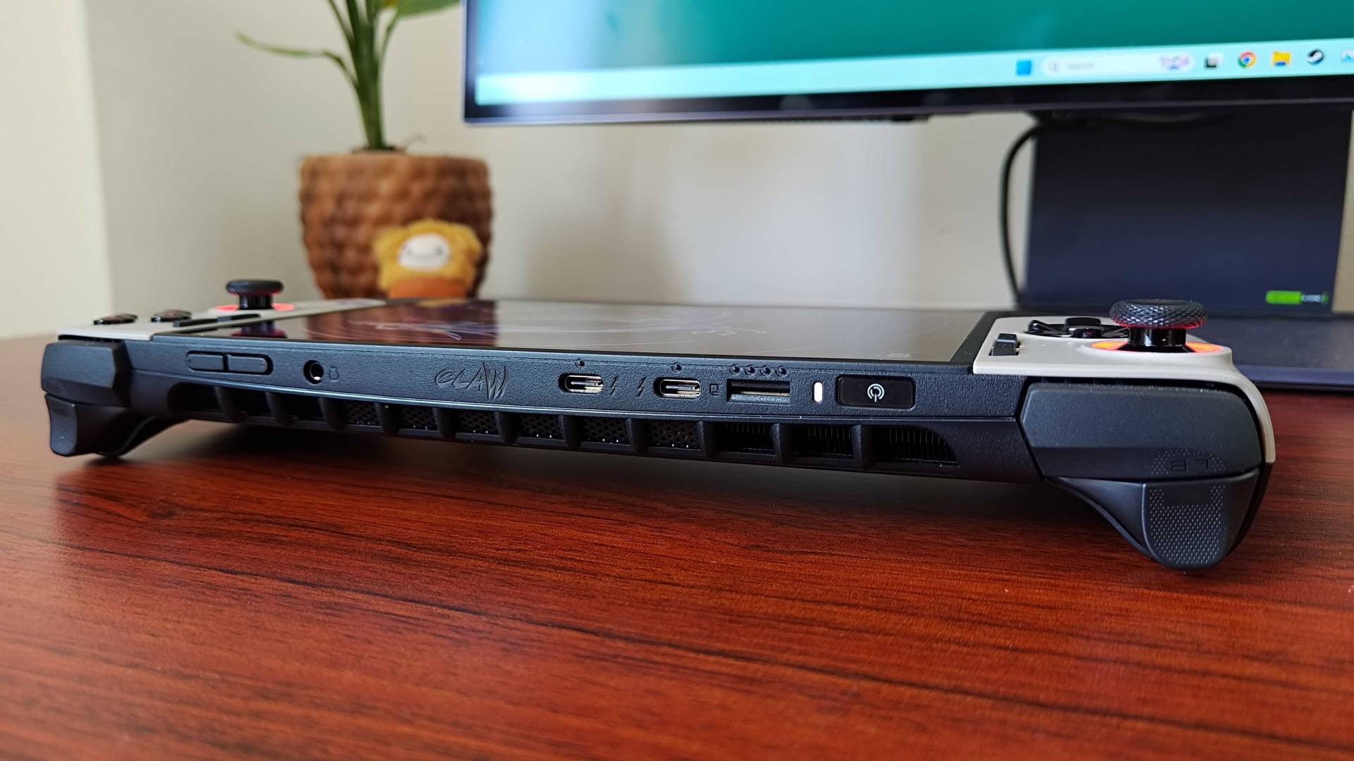 MSI Claw 8 AI+ handheld on woodgrain desk with top of device facing forward and USB ports, volume, and power buttons in view.
