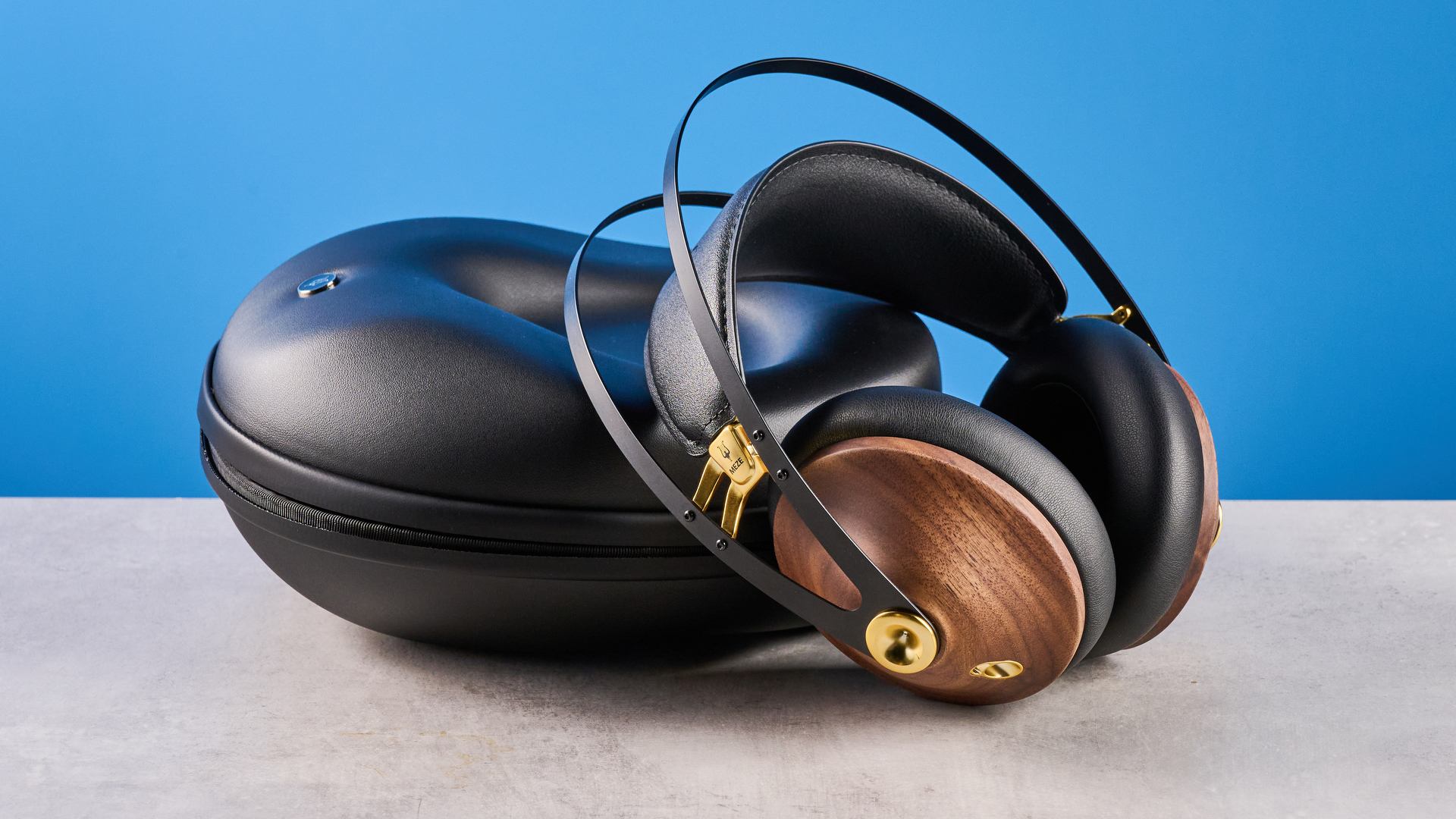the meze 99 classics 2nd gen headphones with walnut finishes and gold touches against the blue tom's guide background