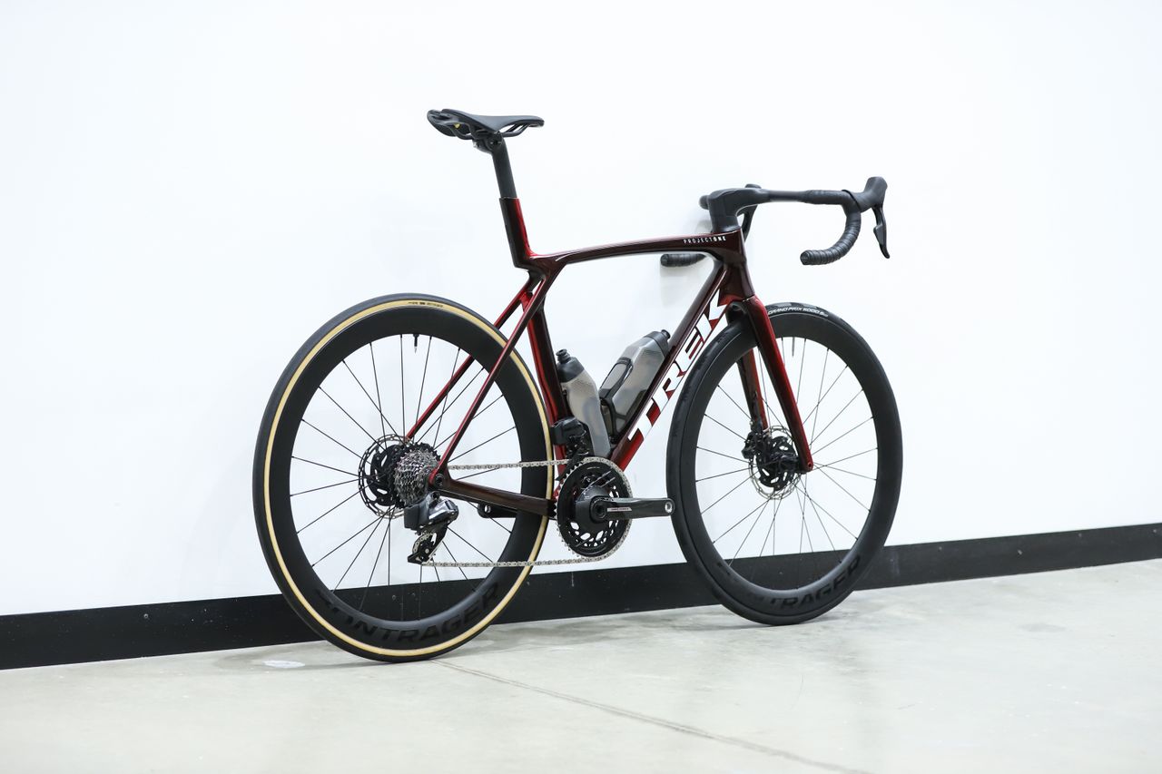 A red Trek Madone SLR 7 (gen 8) stands against a white wall