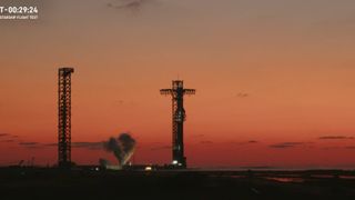 A giant SpaceX Starship rocket on the launch pad just before sunrise with a plume of gas