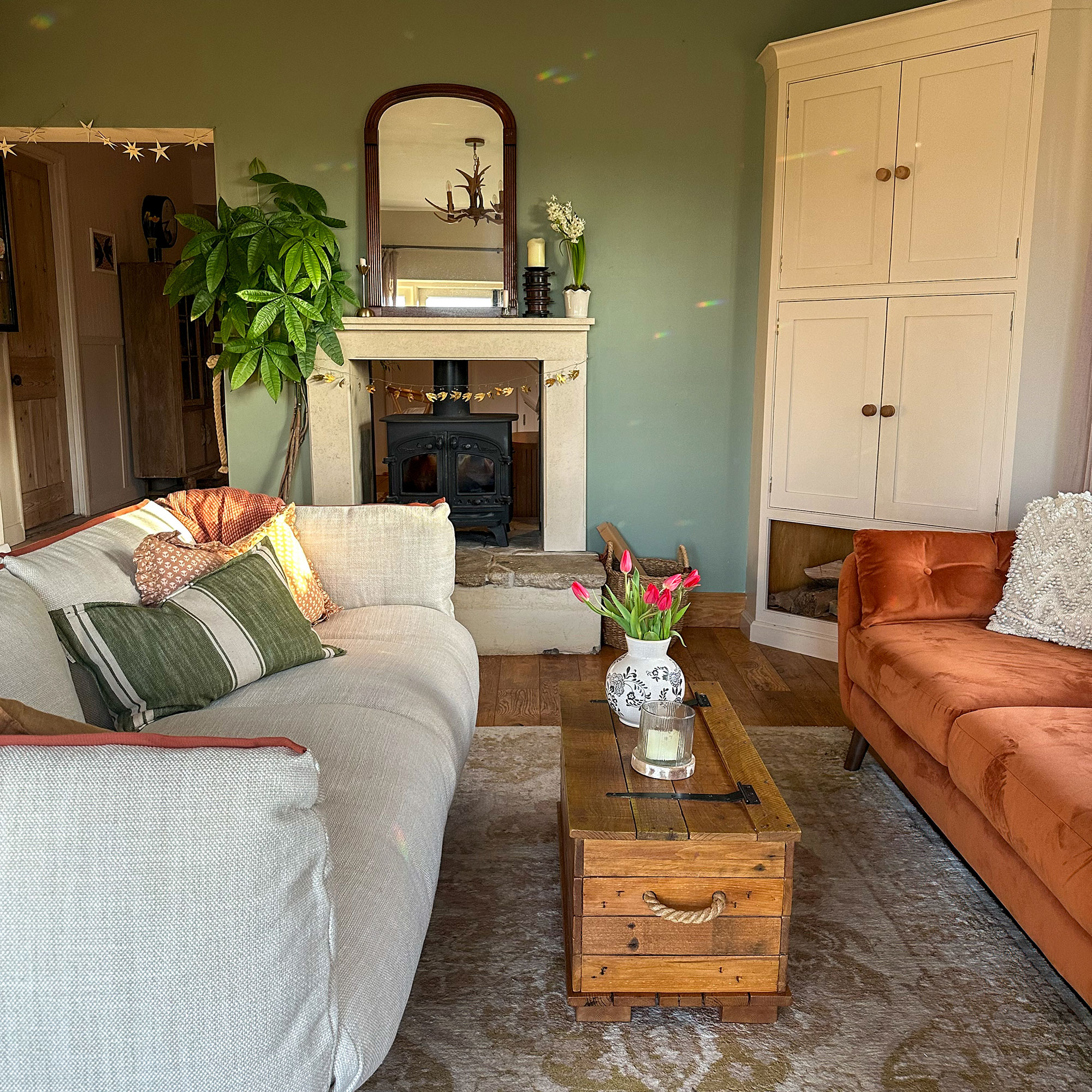 Green living room with cream sofa and orange sofa around wooden chest coffee table and near wood burner