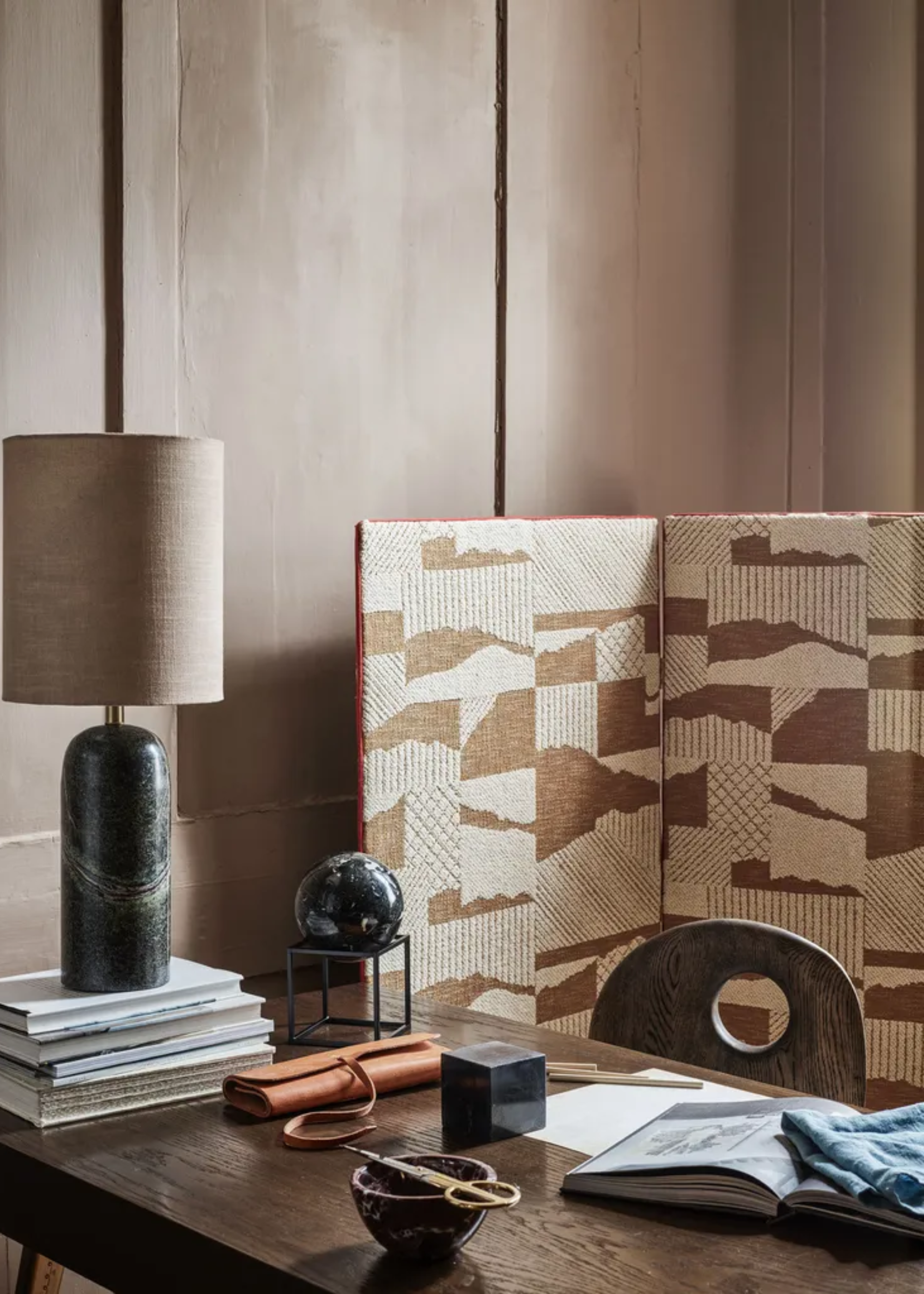 A home office with a wooden table, a table lamp, a patterned room divider and trinkets
