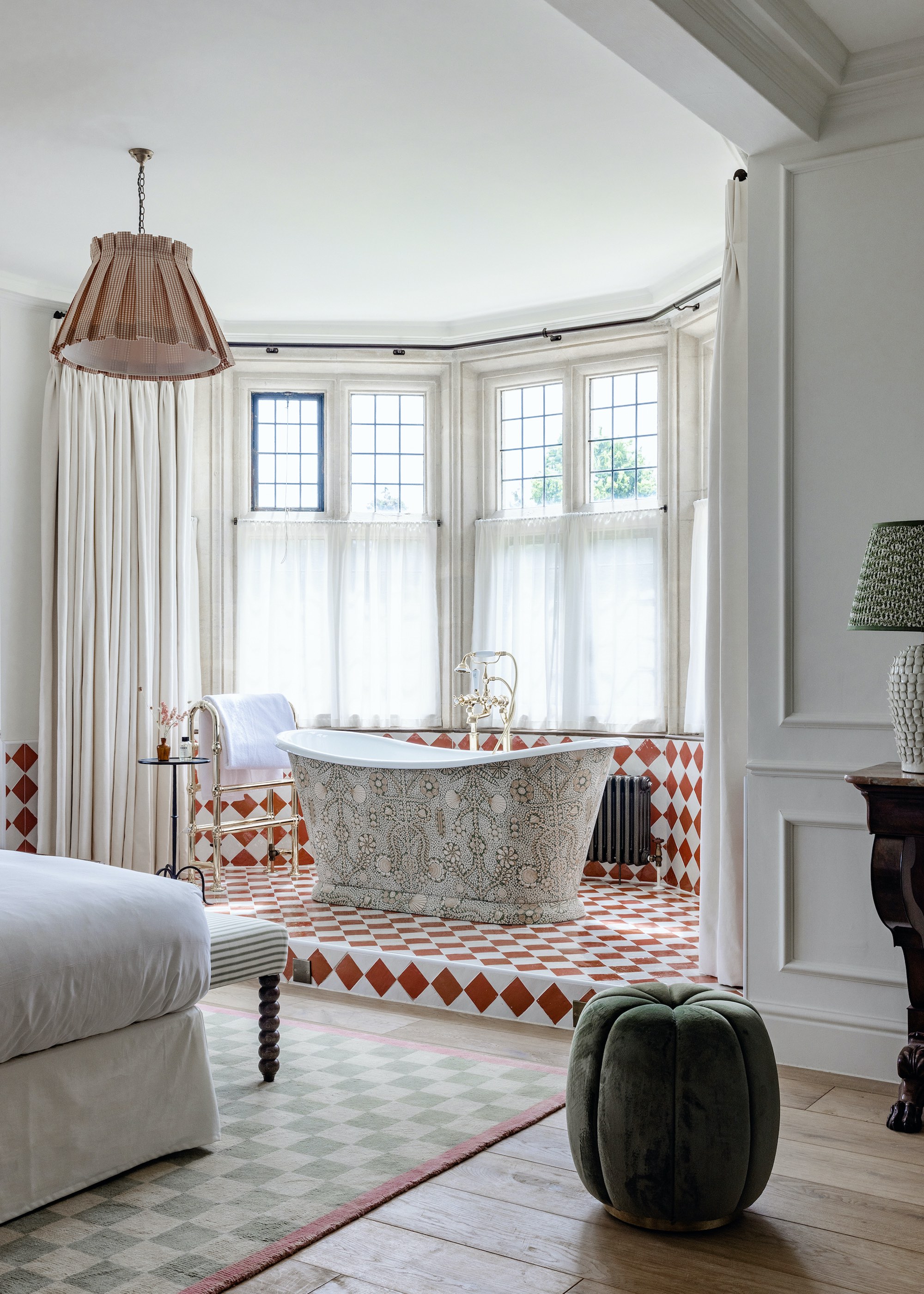 bedroom with bath area clad with red and white tiles. There is also a light shade to match the bath tub tiling and a green and white checkered carpet