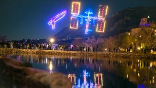 300 drones light up in the shape of a colorful space shuttle and space station over a lake at night