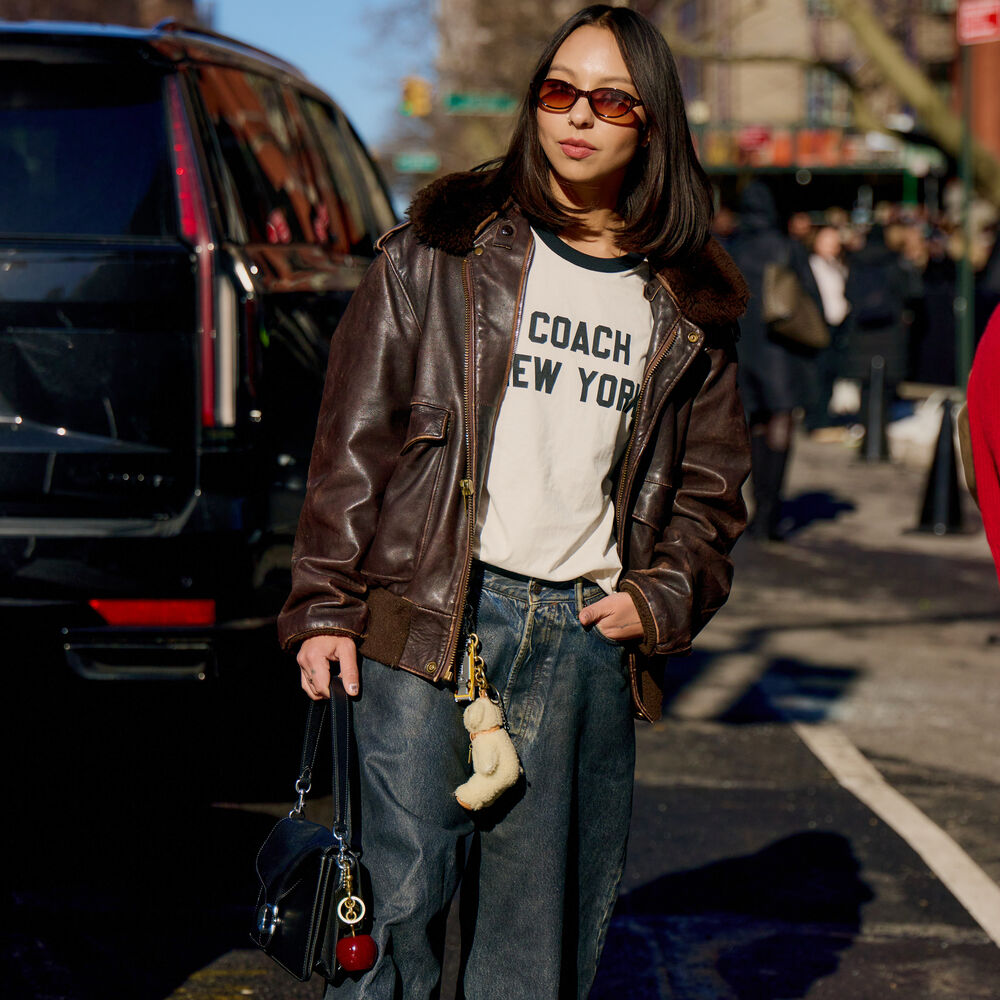 Woman wears brown suede or brown leather while holding a coach bag.