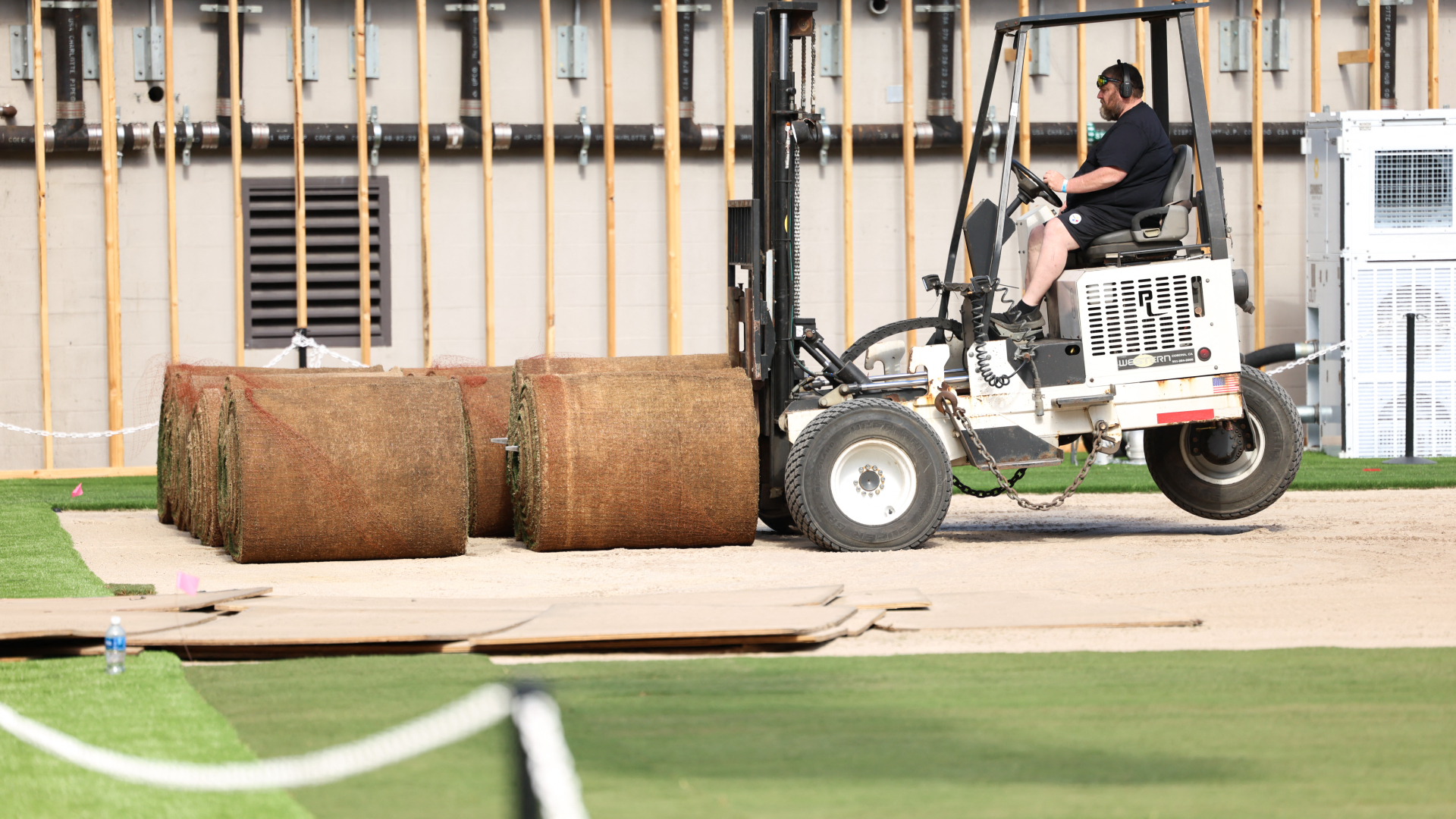 A man in a forklift picks up large rolls of green turf.