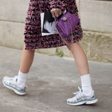 a woman walking down the street wearing a tweed skirt with sneakers and a chanel bag