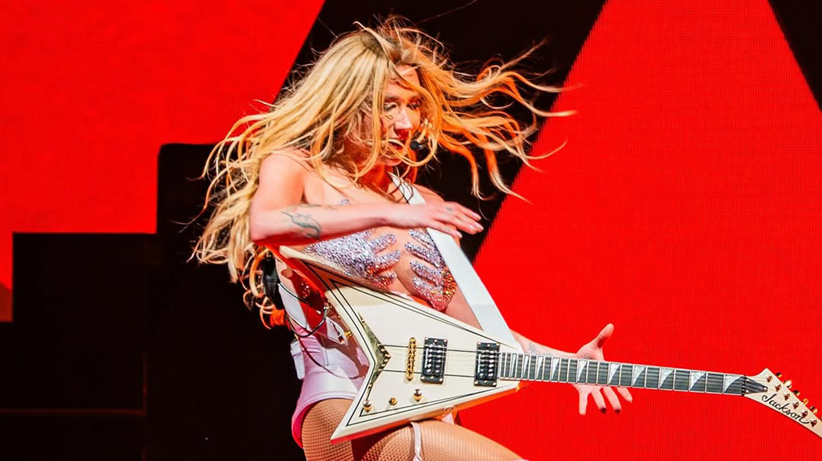 Kesha with a Jackson Rhoads model on stage, with a black and red background