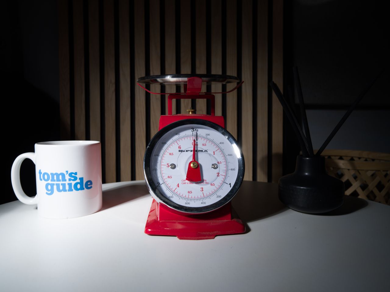 A photo of a set of red scales, with a Tom's Guide mug and a diffuser pot set either side.