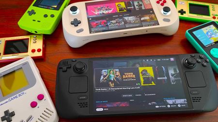 Various gaming handhelds on woodgrain desk including Steam Deck OLED, Ayaneo 2S, Game Boys and Super Pocket.