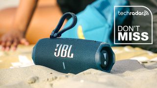 Blue JBL Charge 6 Bluetooth speaker sitting in sand