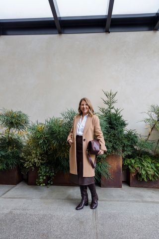 Sandy Koszarek wearing a tan overcoat, white button-down, and chocolate brown skirt.