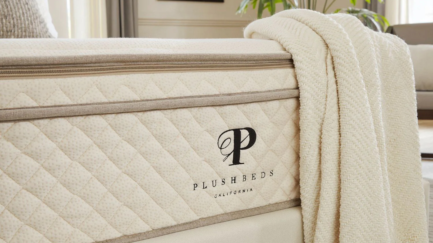 A closeup of the PlushBeds logo on the foot of the PlushBeds Botanical Bliss Mattress, with bedding draped over the end of the bed