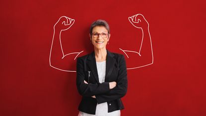 A woman stands against a red background with her arms crossed. Cartoon arms with big muscles are drawn on the red background on either side of her.