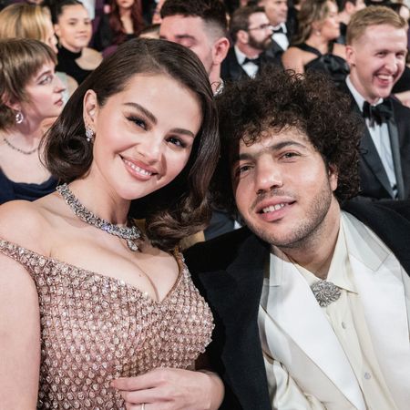 Selena Gomez in a beaded gown and Benny Blanco in a white suit and black coat sitting at the Oscars on March 2, 2025 