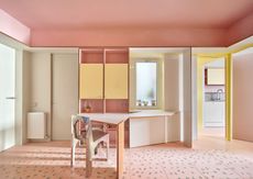 A space with dusty pink walls and floor, and yellow painted cabinet 