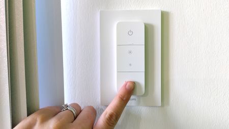 Woman's hand pressing Philips Hue Dimmer Switch on wall