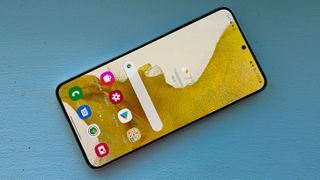En Samsung Galaxy S22 Plus ligger med framsidan vänd uppåt på en blå yta.