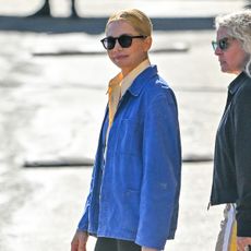 Michelle Williams wearing a blue chore coat, yellow shirt, black skinny pants, and slipper mules in L.A.