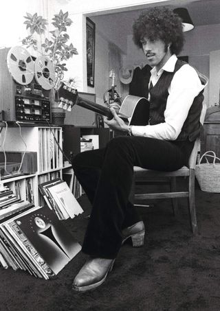 Phil Lynott at home, playing an acoustic guitar with some vinyl records and a reel-to-reel tape machine