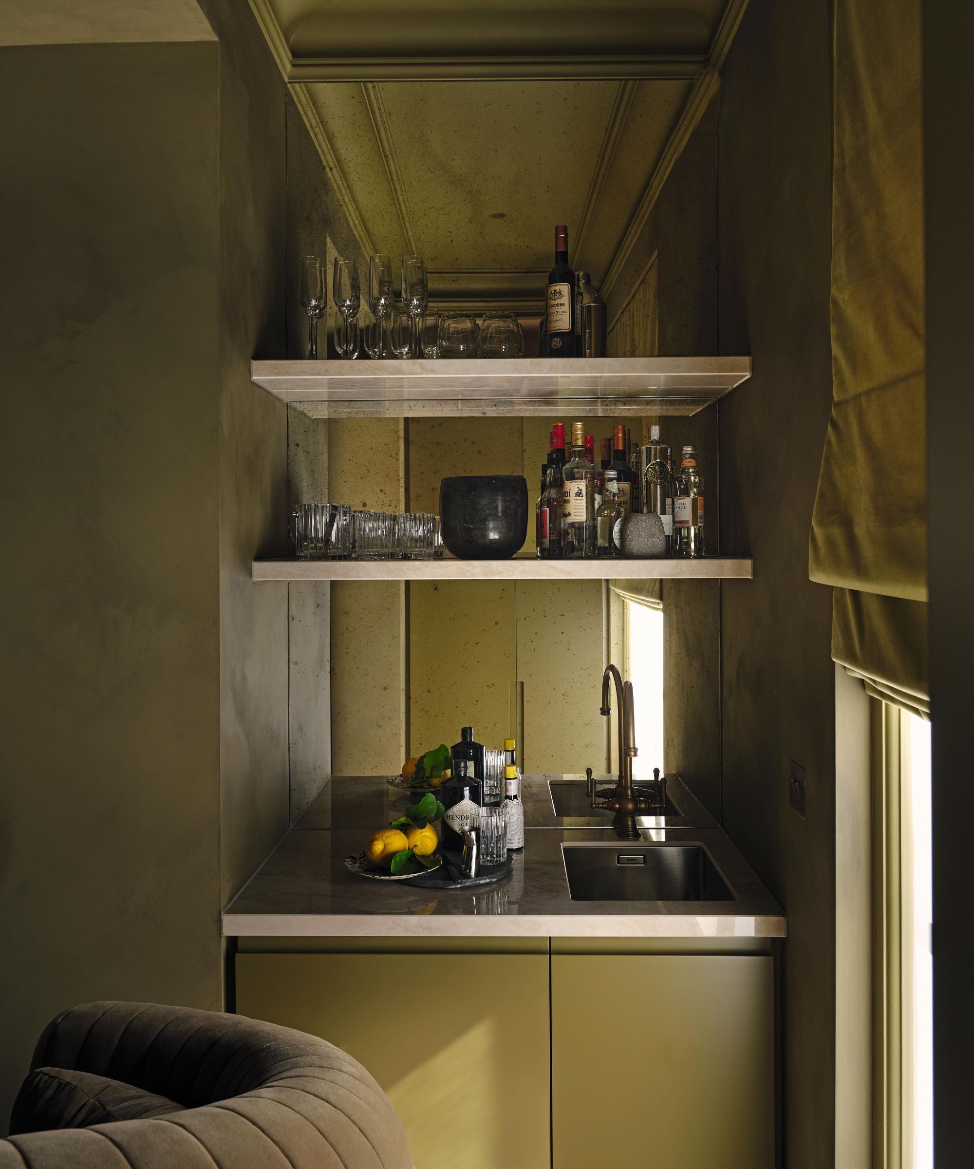 a green limewashed sitting room with a built in mirrored home bar area