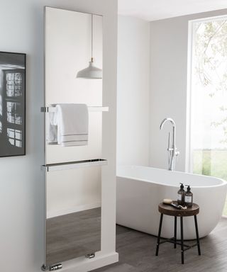 A modern white bathroom with freestanding white tub, wooden stool and mirrored radiator with towel rail