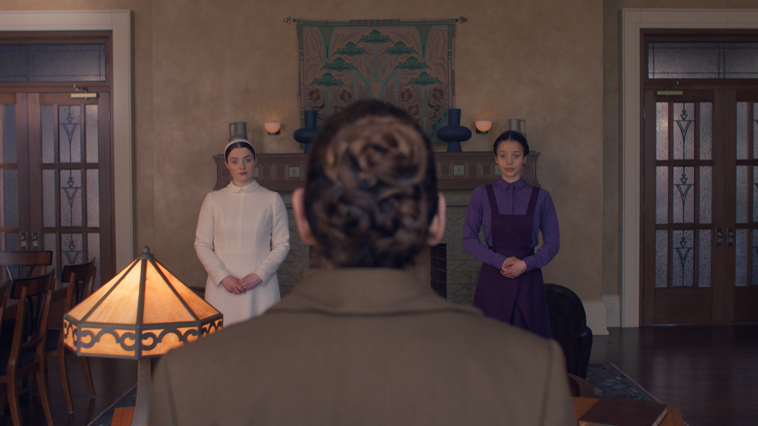 A woman's back is facing the camera as Agnes (Chase Infiniti) and Daisy (Lucy Halliday) look at her from each side.