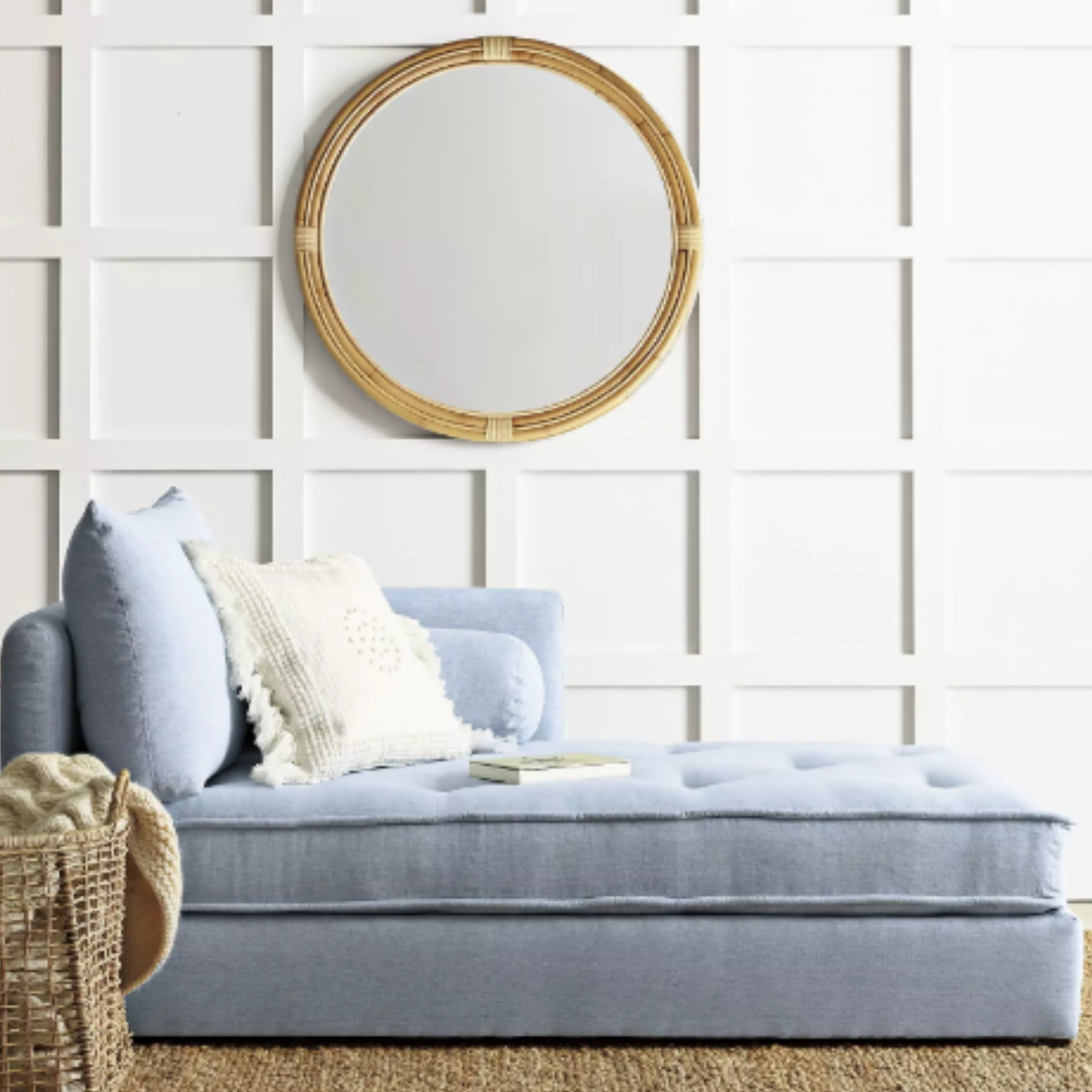 A blue chaise with pillows and a circular mirror behind