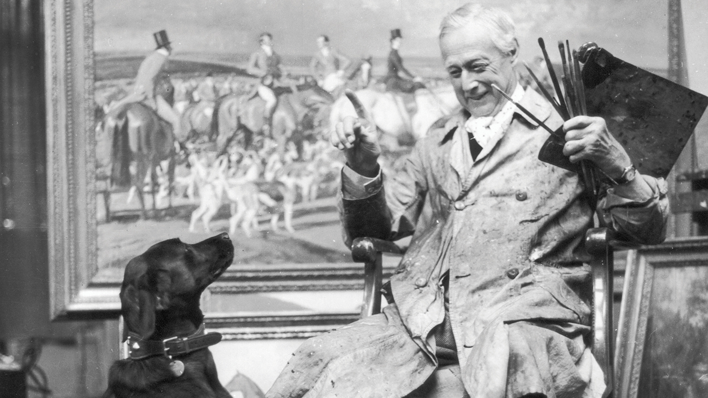 Sir Alfred James Munnings (1878 - 1959), the English painter and President of the Royal Academy playing with his dog in front of one of his works in his studio. (Photo by Baron/Hulton Archive/Getty Images)
