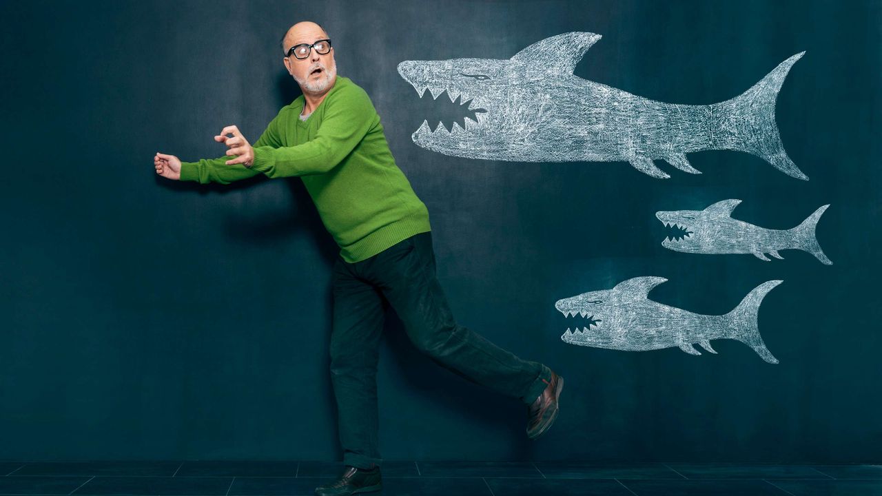 A man, looking over his shoulder, runs away from sharks drawn on a chalkboard.