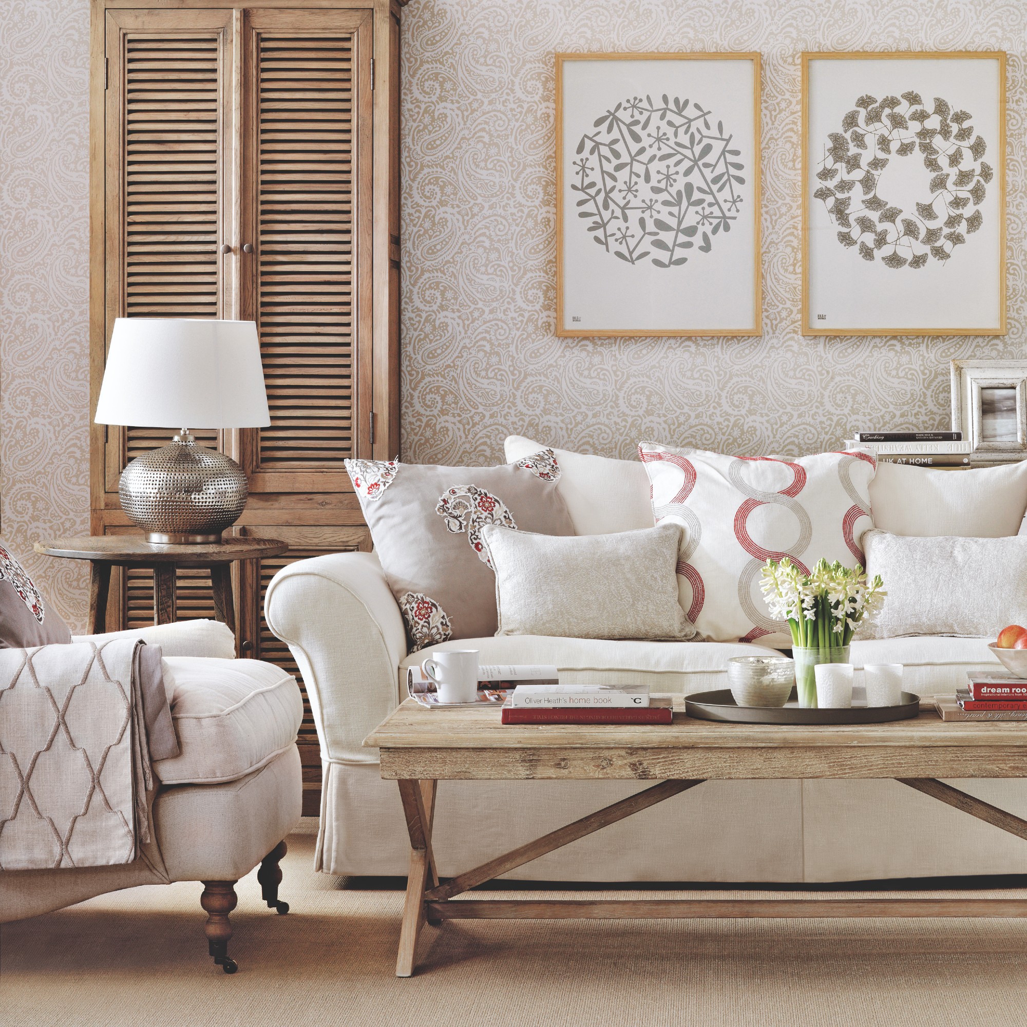 A neutral living room with a cream sofa and many cushions and a matching armchair