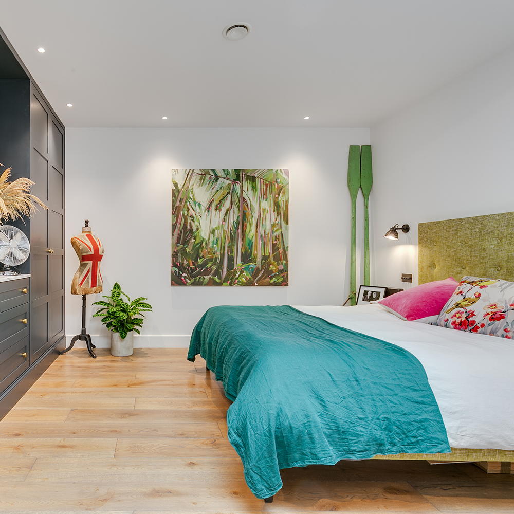 bedroom with white wall bed with designed cushion frame on wall and wooden flooring