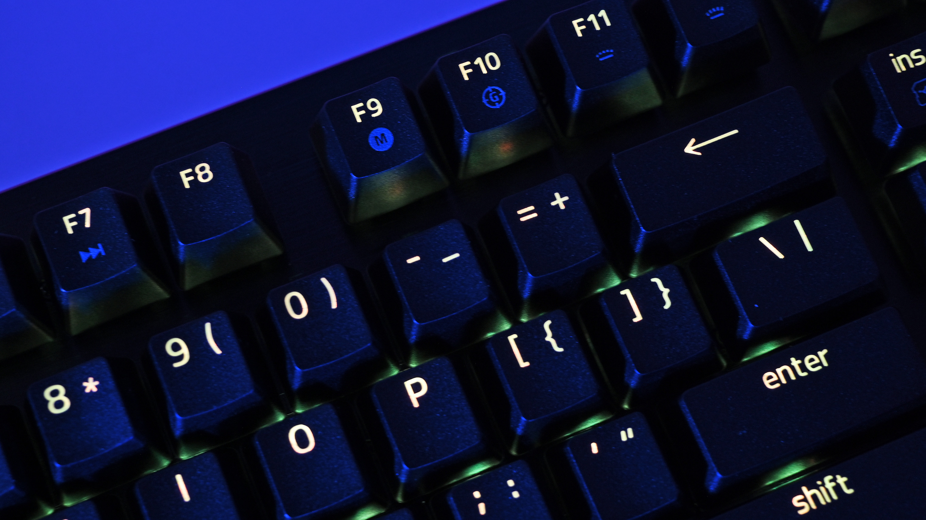 Close-up of a dimly Razer Huntsman V3 Pro TKL 8KHz with glowing symbols on black keys, including F7 to F11, and numbers 8 to 0. Blue light creates a futuristic feel.
