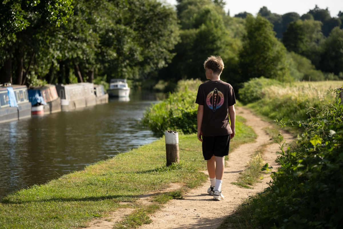 Viltrox AF 90mm F2.2 EVO lens image gallery: adolescent boy walking along a towpath, there are canal boats in the river, it's golden hour