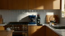 Image of a navy blue La Marzocco machine on a white kitchen countertop with wooden cabinetry. There is a black coffee grinder and scale next to it.