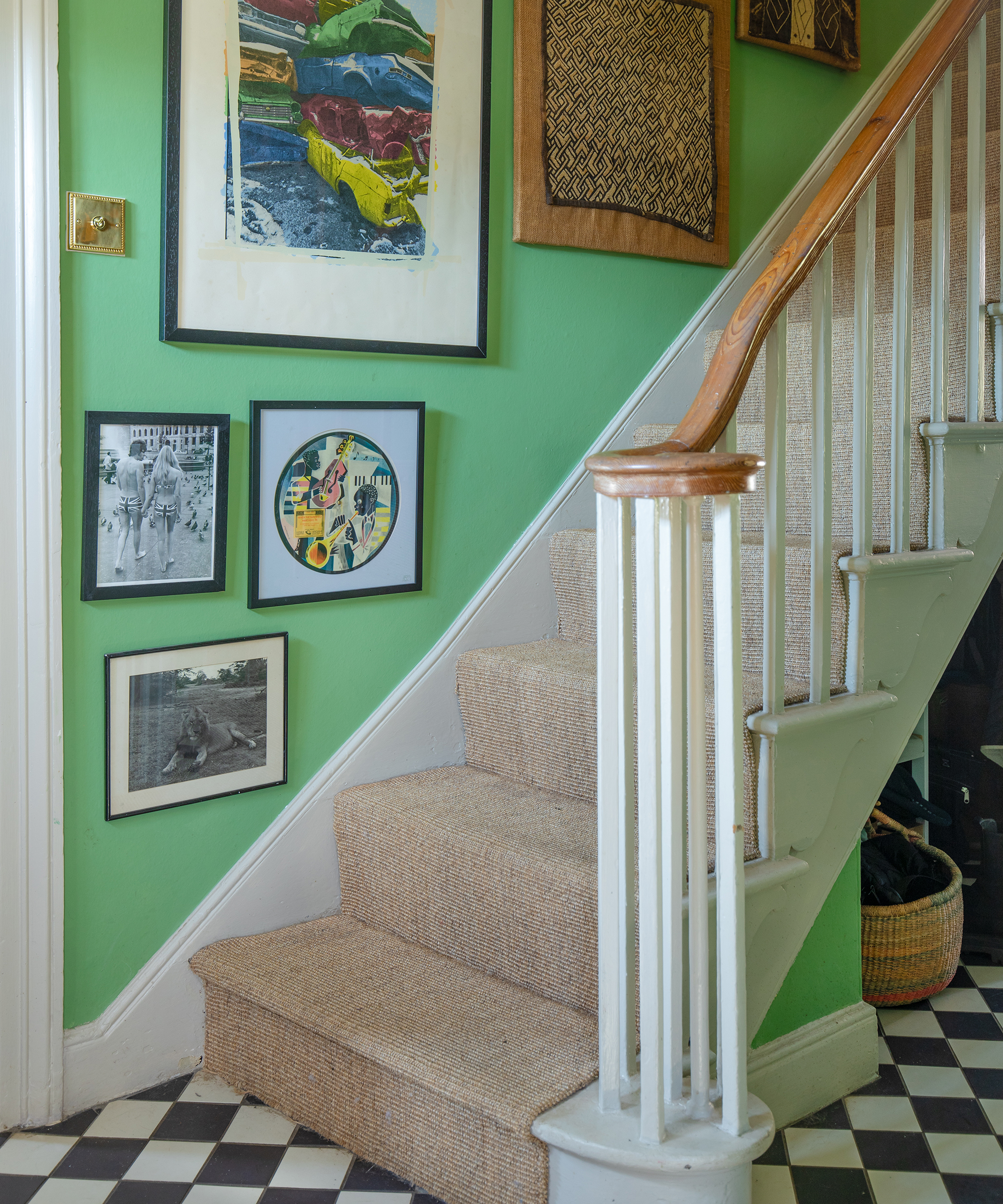 hallway with vibrant green walls, black and white chequered floor, seagrass carpet on stairs and artworks